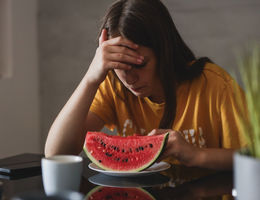 teen with hand on head in frustration while sitting at table in front of slice of watermelon