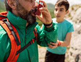 If you answer “yes” to any of the Rule of Two questions, the Advanced Lung Disease Center can evaluate you and advise you on a care plan at their clinic. an inhaling himself with asthma inhaler, while his worried son giving him support, during their hike stock photo