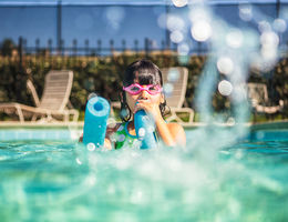 child in goggles playing in pool with foam floaty