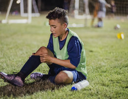Young soccer player sitting on the grass nursing an injury.