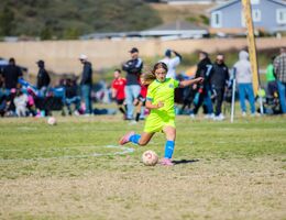 Young girl kicks soccer ball at sports game.