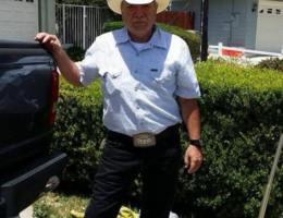 A person wearing a white cowboy hat stands beside a pickup truck on a sunny residential street.