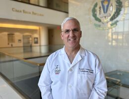 Dr. Randall Fortuna wearing white coat in hallway smiling