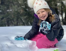 Young girl in beanie sitting on snow making snowballs