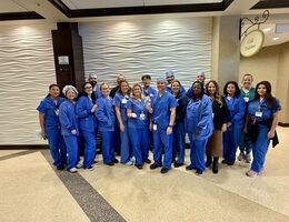 A large group of people in medical scrubs posing together in a hospital lobby.