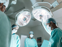 Study reveals young children with perforated appendicitis benefit most from prompt surgery removing appendix Four health workers wearing surgery clothes and masks, standing face to face in operation room with lamps on top.