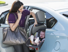 Young Hispanic woman (20s) traveling with baby girl (6 months), in car seat, talking on mobile phone.