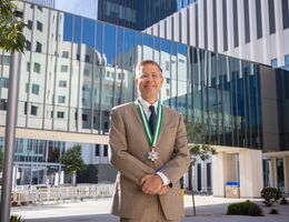 Dr. Forrest Jellison standing outside in fornt of the LLU Medical Center building in a tan suit wearing a medal