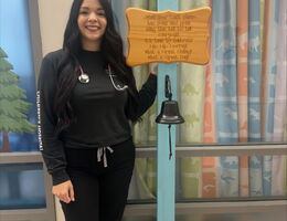 Heather Kono stands by cancer free bell on pediatric cacner unit