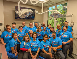 A group of people in blue shirts stand together in a dental office
