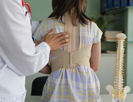 Doctor adjusts spine brace on young patient in a clinical setting, focusing on health and wellness