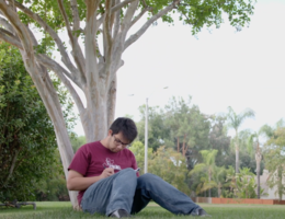 Tyler Rojanaroj sits at the base of a tree writing music.
