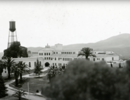 black and white photo of a university campus, hills in the background, trees in the foreground