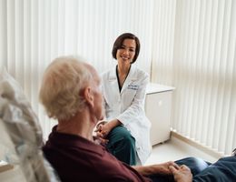 Asian female doctor sitting in a doctor's office with a male, white-haired man