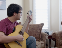 Tyler Rojanaroj sits on a couch playing guitar