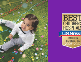 young boy smiles while sitting on grass with confetti, US News badge on purple background