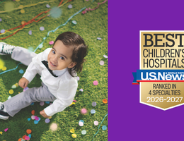 young boy smiles while sitting on grass with confetti, US News badge on purple background