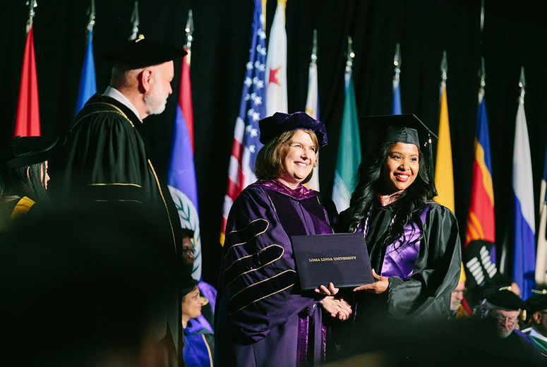 A graduate smiles as she receives her diploma from President Hart, Dean Marshak.