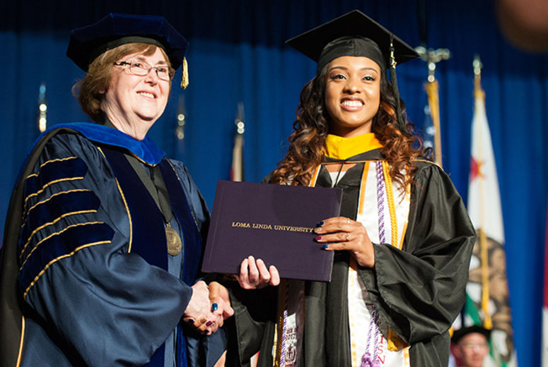 A School of Nursing graduate shares a handshake and smile with Dean Elizabeth Bossert, PhD.