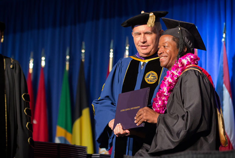 President Richard Hart, MD, DrPH, and Dean of the School of Religion Jon Pauline, PhD, share smiles with this graduate receiving his diploma.